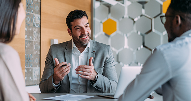 Three people in business attire have a meeting in a modern office. As one man discusses how to archive bank records, the other two listen attentively across the table.