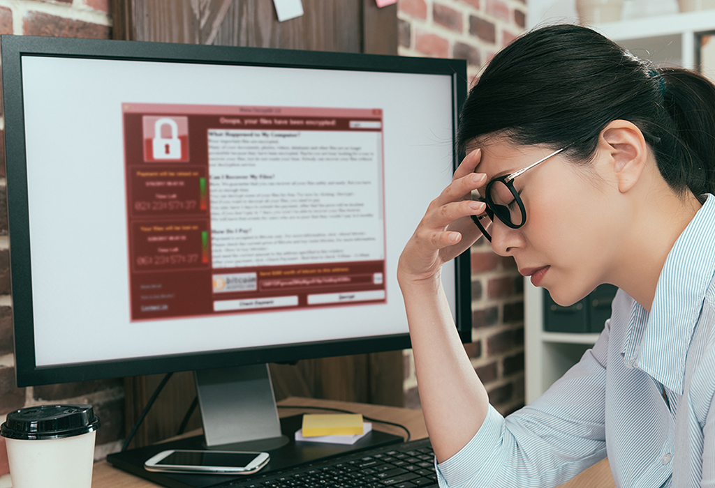 A woman looking stressed while viewing a computer screen displaying a ransomware recovery notification.