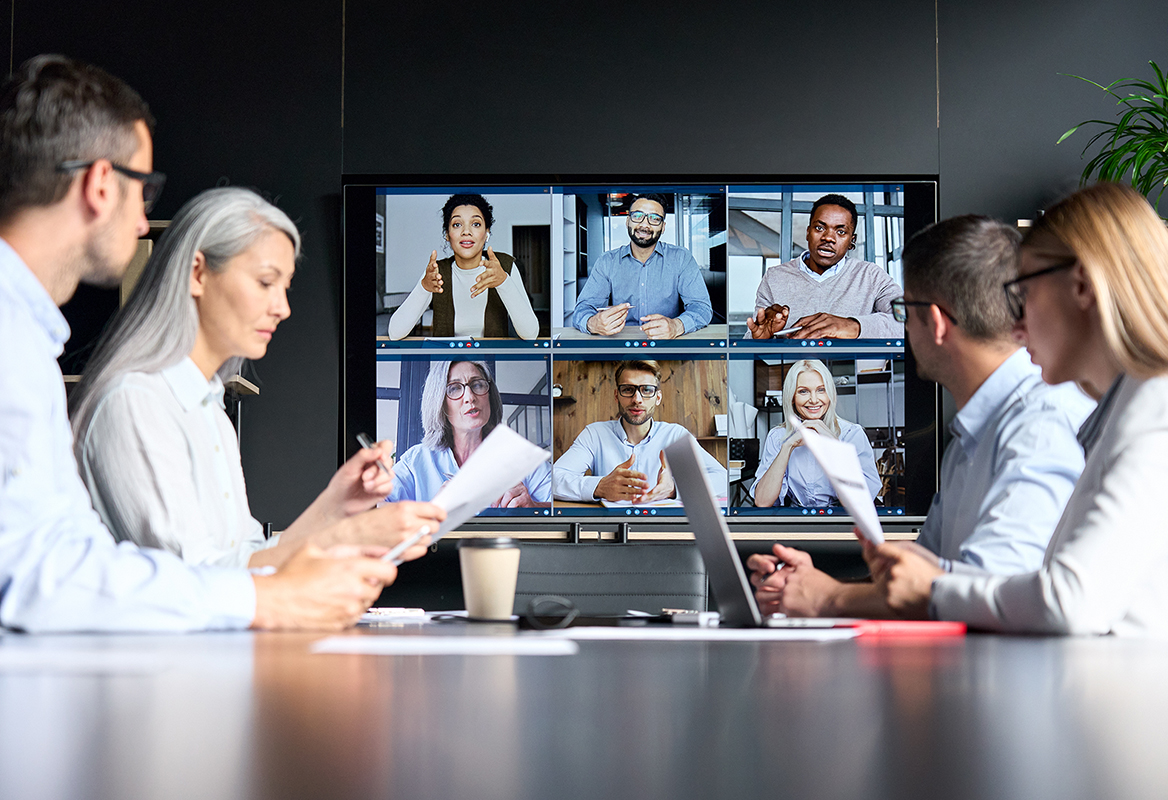 Business professionals in a conference room engaging in digital collaboration with remote colleagues displayed on a large screen.