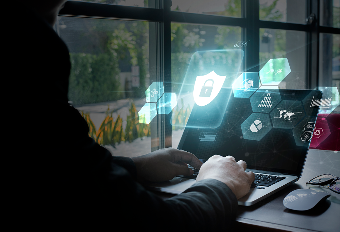 A person working on a laptop with cybersecurity icons and graphics emanating from the screen in a modern office setting.