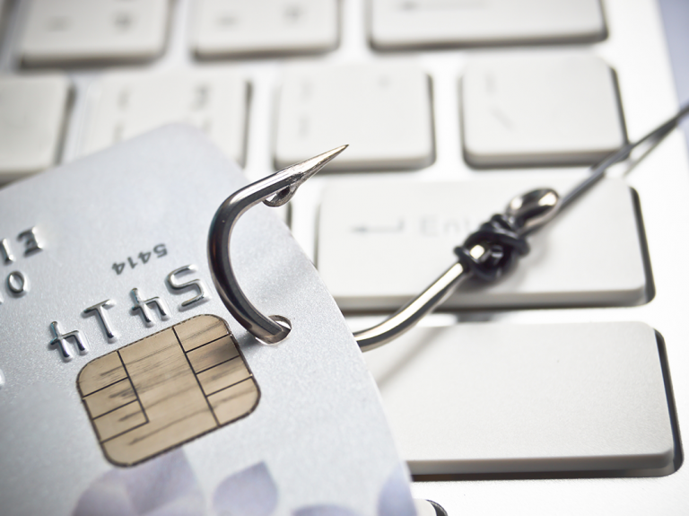 A close-up image of a credit card with a fishing hook attached, symbolizing potential financial phishing or fraud.