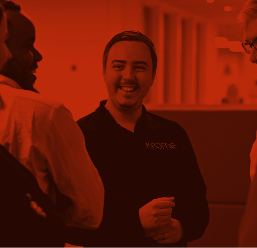 A man smiling and conversing with colleagues in a red-tinted office environment.