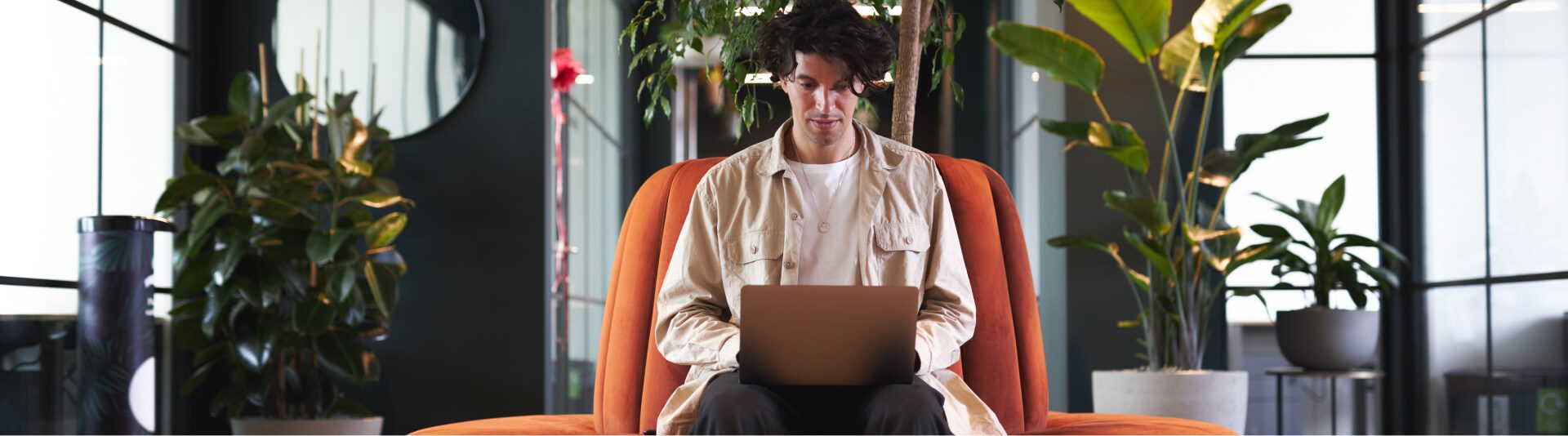 Man sitting in an orange chair using a laptop in a modern office space with Darktrace Consultancy plants around.