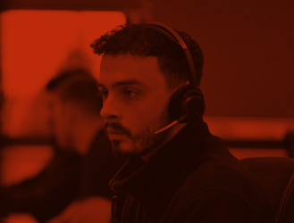 A man wearing headphones focuses intently on his computer screen in a room illuminated with red lighting, working at a Managed Services Provider.