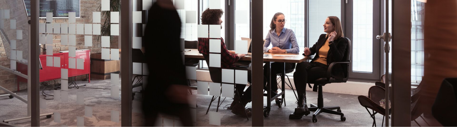 Two professionals seated at a table discussing, with blurred figures passing by in a modern office setting with glass partitions of a Palo Alto Networks Partner.