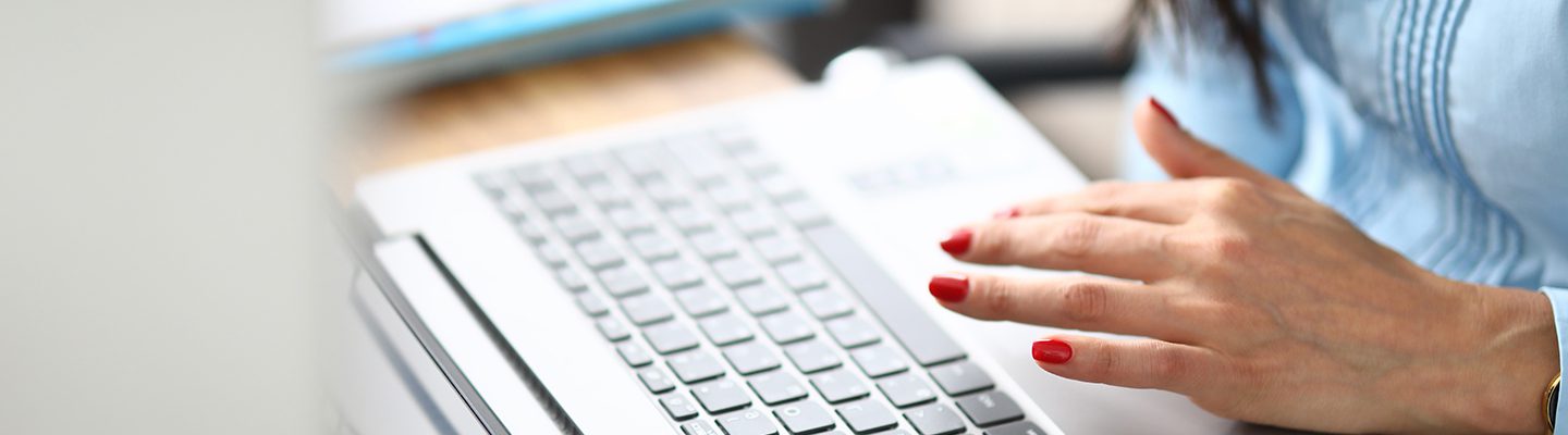 A close-up of a Delinea Partner typing on a laptop keyboard, focusing on her hand with red-painted nails.