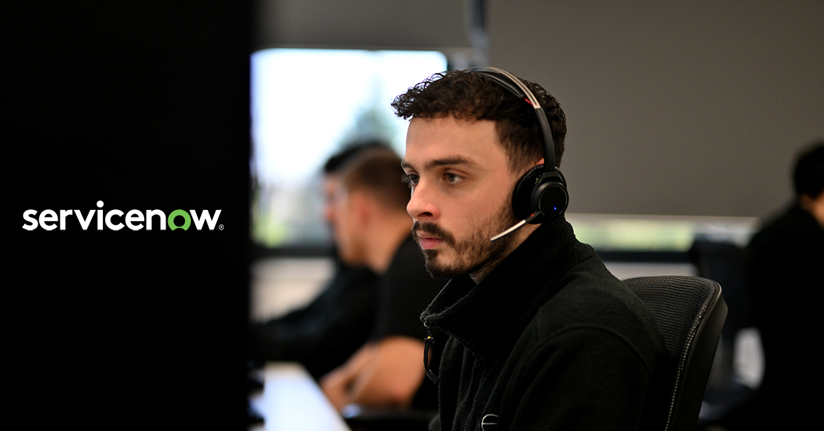 A man wearing a headset works diligently at a computer, showcasing the ServiceNow logo in the background.