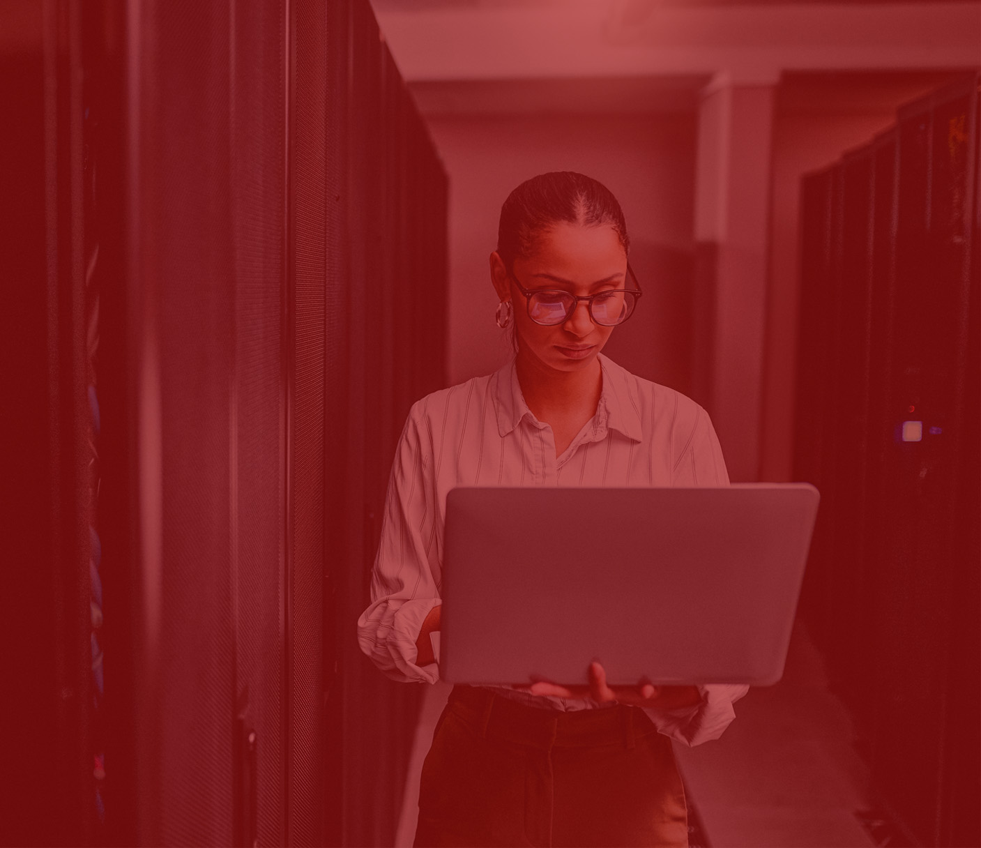 A person wearing glasses uses a laptop while standing in a server room lined with computer racks, preparing for the Tech Drop-In Masterclass.