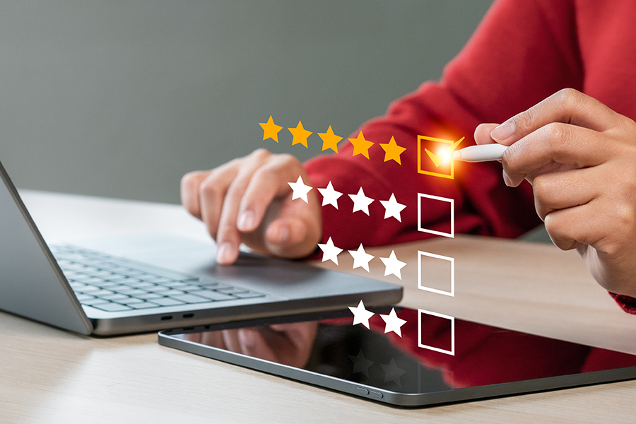 A person uses a stylus to give a five-star rating on a virtual interface, reflecting Krome Client Satisfaction, with a laptop and tablet on the desk.